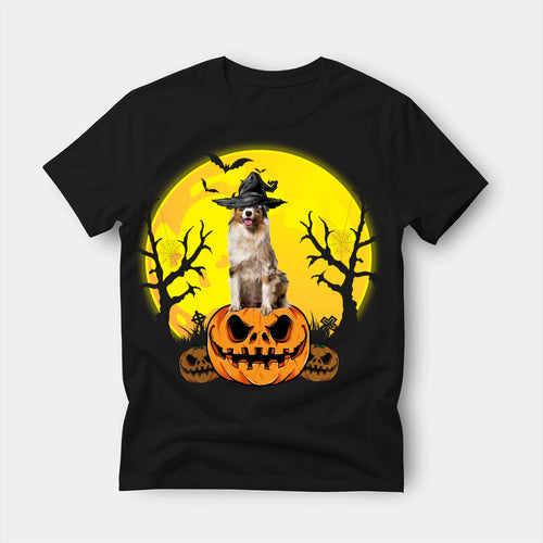 Black t-shirt printed with an Australian Shepherd in a witch's hat sitting on a carved Halloween pumpkin, with bats and bare trees under a full moon